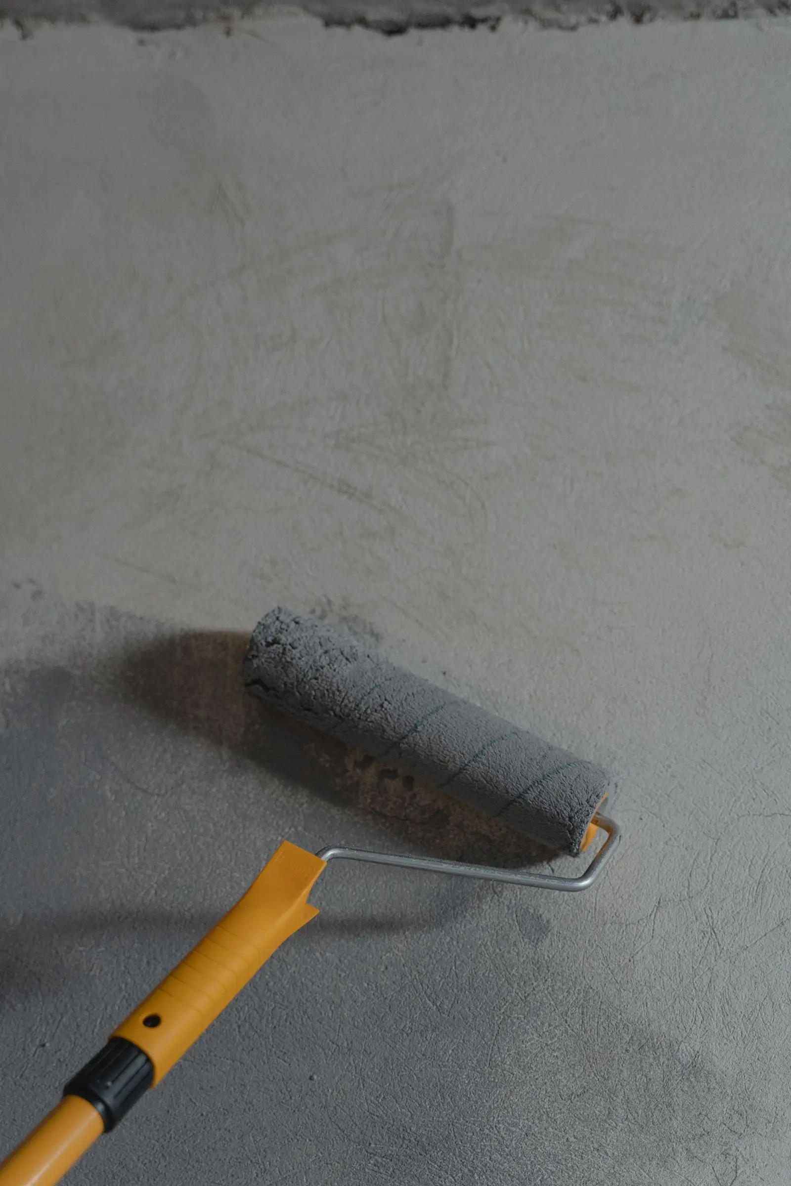 Rodillo con pintura gris sobre un muro recién estucado